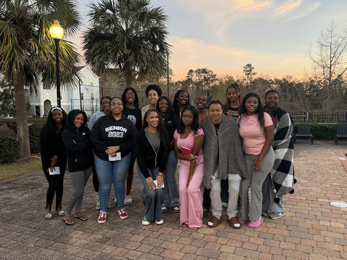 EFF women gathered outdoors at dusk beneath palm trees, one holding a pink Bible
