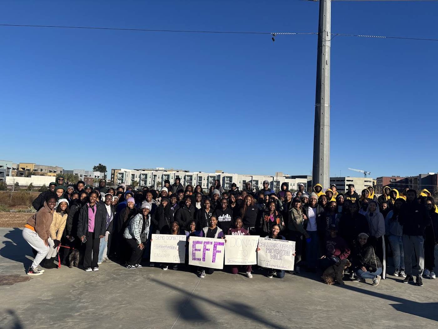 More than a hundred students gathered under a blue sky with signs reading EFF and College Dropout Prevention Walk